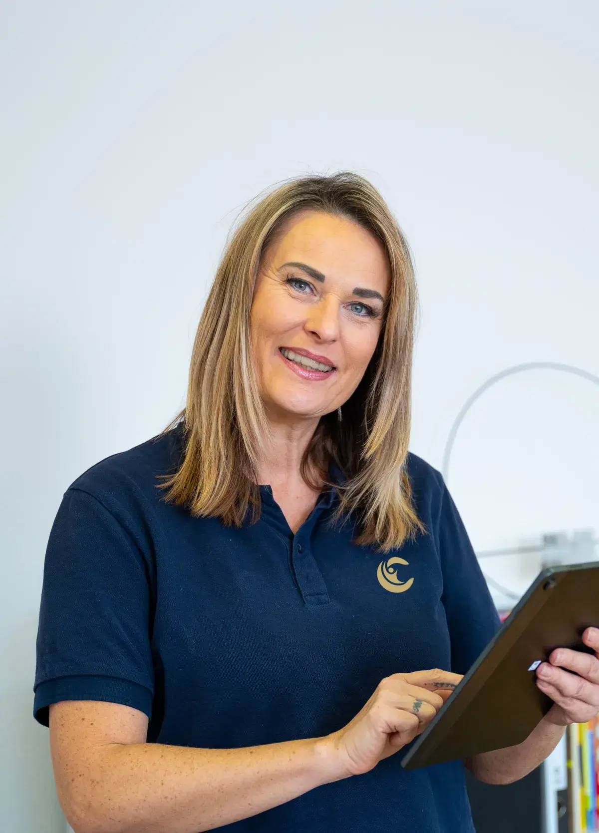 Lächelnde Therapeutin im Curano-Poloshirt mit einem Tablet